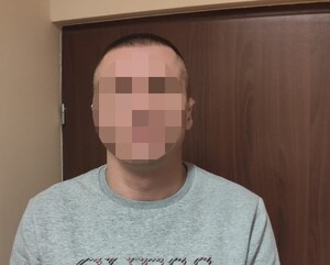 Zatrzymany mężczyzna ubrany w szarą bluzę stojący przodem do zdjęcia