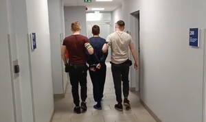 dwóch niumundurowanych policjantów prowadzi przez korytarz komisaraitu zatrzymanego