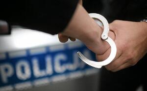 Ręka na którą są zakładane kajdanki. W tle napis Policja