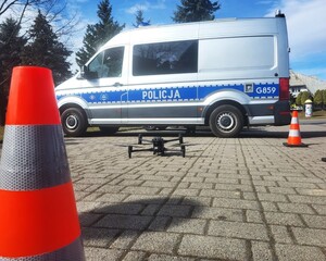 Oznakowany radiowóz, przed nim  startujący dron policyjny
