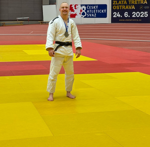 Stojący na macie koloru żółtego zawodnik judo w sportowym stroju z medalem