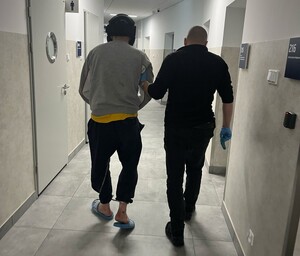 nieumundurowny policjant prowadzi zatrzymanego mężczyznę  z założonymi kajdankami zespolonymi przez korytarz komisaraitu