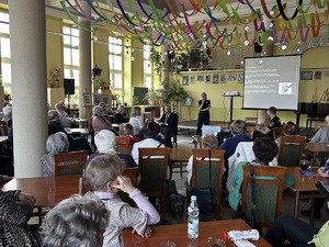 uczestnicy spotkania przy stołac słuchają prelekcji