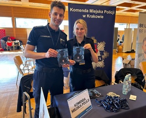 Pamiątkowe zdjęcie policjanta i policjantki na tle stoiska z ulotkami dla kandydatów