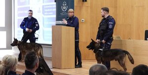policjantka przy pulpicie obok dwa j policjanci z psami służbowymi