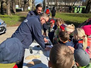 Dwaj policjancirozmawiaja z dziećmi przy policyjnym stoisku