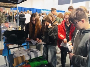 Trzy dziewczyny i chłopak, którzy czytają broszury informacyjne. W tle tłum ludzi.