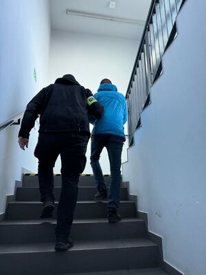 Policjant prowadzi zatrzymanego meżczyznę  po schodach