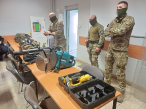 Trzej funkcjonariusze służby więziennej prezentują sprzęt wykorzystywany w służbie