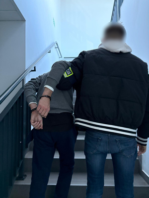 Nieumundurowany Policjant prowadzi po schodach zatrzymanego mężczyznę