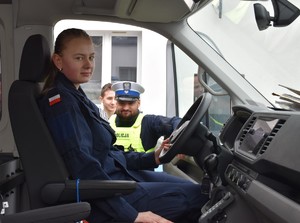 uczennica siedząca w radiowozie obok stoi policjant