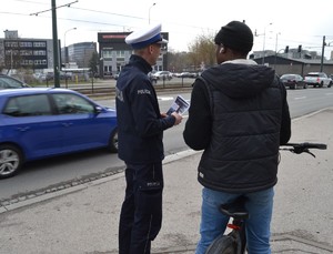 Policjant trzyma w ręku ulotki i rozmawia z rowerzystą