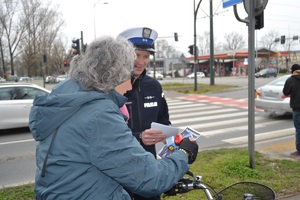 Policjant wręcza rowerzystce ulotkę oraz światełko