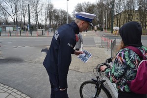 Policjant wręcza rowerzystce ulotkę