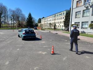Policjant na placu manewrowym idzie za jadącym samochodem.