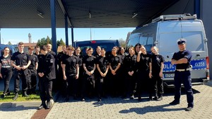 Uczniowie klas o profilu policyjnym, w czarnych mundurach. Po prawej stronie policjant ruchu drogowego oraz oznakowany radiowóz.