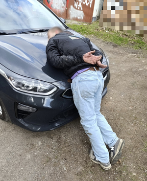 Zatrzymany na masce samochodu z kajdankami założonymi na ręce trzymane z tyłu