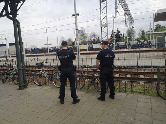Umundurowany policjant oraz funkcjonariusz Straży Ochrony Kolei przy torach kolejowych