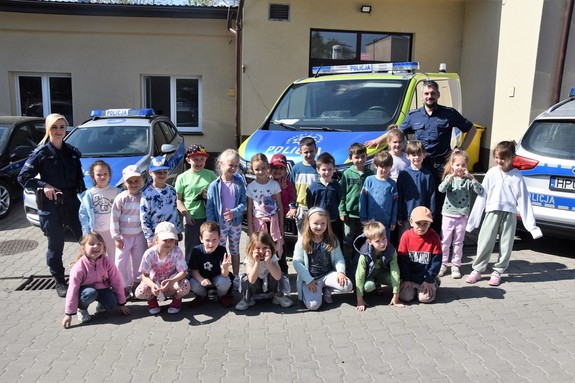 Zdjęcie grupowe. Funkcjonariusze oraz dzieci biorące udział w prelekcji na tle policyjnych radiowozów