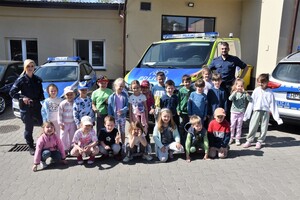 Zdjęcie grupowe. Funkcjonariusze oraz dzieci biorące udział w prelekcji na tle policyjnych radiowozów
