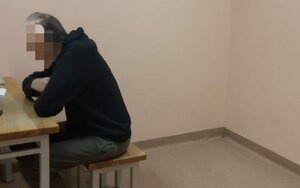 Zatrzymani siedzi przy stoliku w policyjnym areszcie