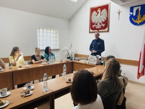 Policjant podczas spotkania omaiający temat i połozona przed nim walizka profialktyczna