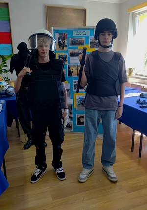 Dwóch chłopaków ubranych w elementy umundurowania policyjnego. W tle gazetki.