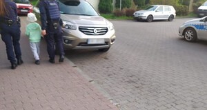 mały chłopiec idący chodnikiem w towarzystwie dwójki policjantów