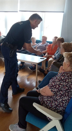 Umundurowany policjant przed nim siedzą osoby starsze
