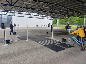 umundurowani policjanci, chłopiec na rowerze przed mobilnym miasteczkiem drogowym