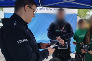 umundurowany policjant przekazuje ulotki uczniom