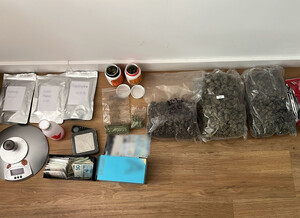 zabezpieczony susz roślinny w foliowych opakowaniach, plastikowe pojemniki z suszem roślinnym, trzy opakowania w srebrnym kolorze, gotówka oraz waga elektroniczna