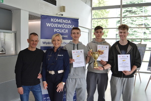 Policjantka wraz z uczestnikami turnieju trzymającymi w ręku puchar i dyplomy
