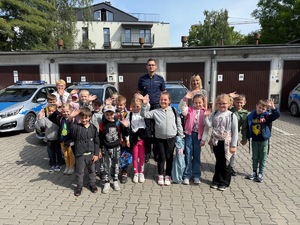zdjęcie grupowe uczniów z policjantem na tle radiowozów oznakowanych