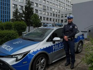 umundurowany policjant stojący przed oznakowanym radiowozem