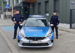 Dwaj policjanci stojący obok radiowozu.