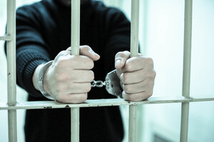 Mężczyzna stoi za kratami i dłońmi trzyma kraty.