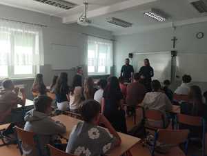 Umundurowani policjanci stojący w klasie przed uczniami.