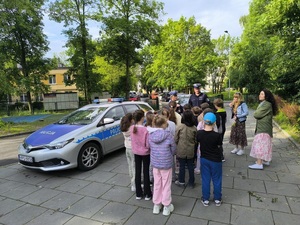Policjanci przy radiowozie omawiają z dziećmi zasady bezpieczeństwa.