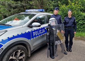 Dziecko w elementach policyjnego umundurowania razem z policjantami przy radiowozie.