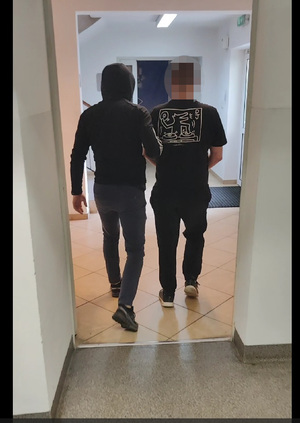 Policjant prowadzi zatrzymanego 27 latka