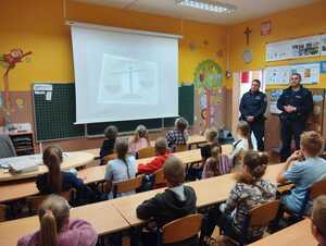 Dwóch policjantów w sali lekcyjnej prowadzi zajęcia z dziećmi.