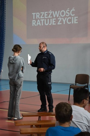 Policjant stoi razem z uczniem w sali.
