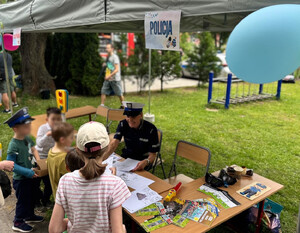 grupa dzieci w towarzystwie policjantki przy policyjnym stoisku profilaktycznym