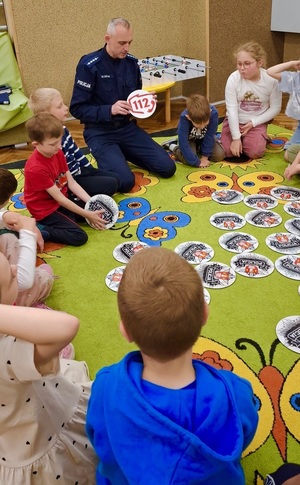 Policjant pokazuje dzieciom numer alarmowy.