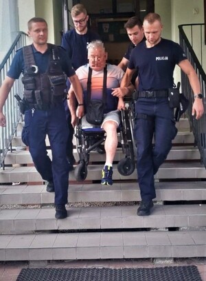Policjanci znoszą ze schodów mężczyznę  z niepełnosprawnością ruchową