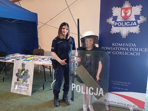 Policjantka z chłopcem ubranym w zestaw ochronny policjanta przy stoisku policji