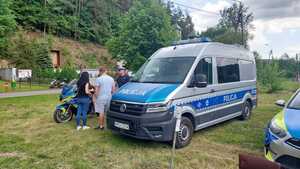 Umundurowany policjant obok radiowozu oznakownaego i motoru policyjnego