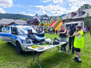 Policjant i dwie dziewczyny oglądające wyposażenie policyjne. W tle radiowóz.