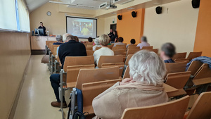 Seniorzy siedzący na sali wykladowej, słuchający policyjnej prelekcji